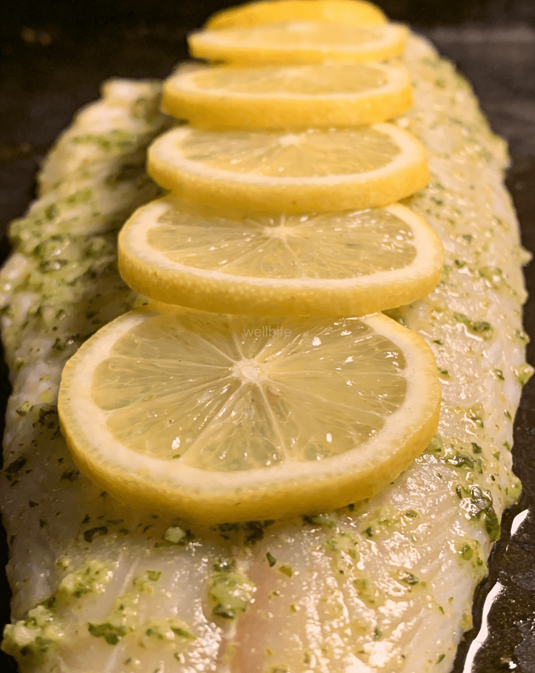 Brushing salmon with herb sauce and topping with lemon