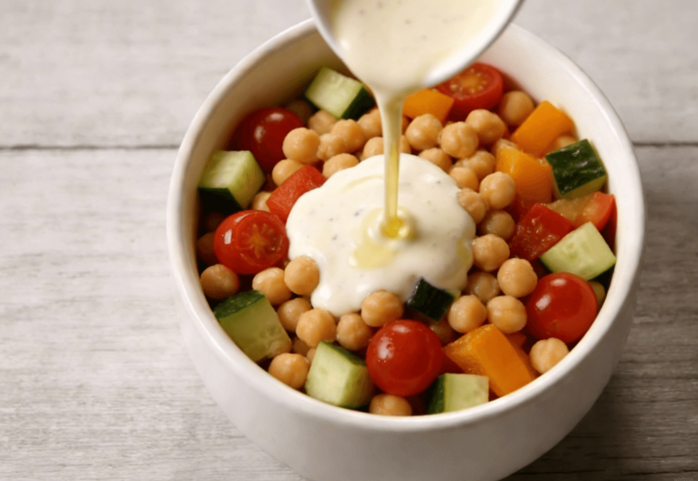 All salad ingredients being tossed together with dressing in a large bowl